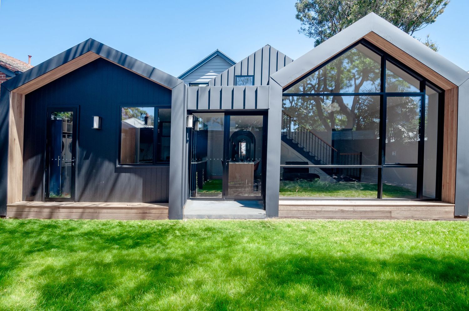 Contemporary dark blue and gray house exterior with geometric gabled design and large glass windows.