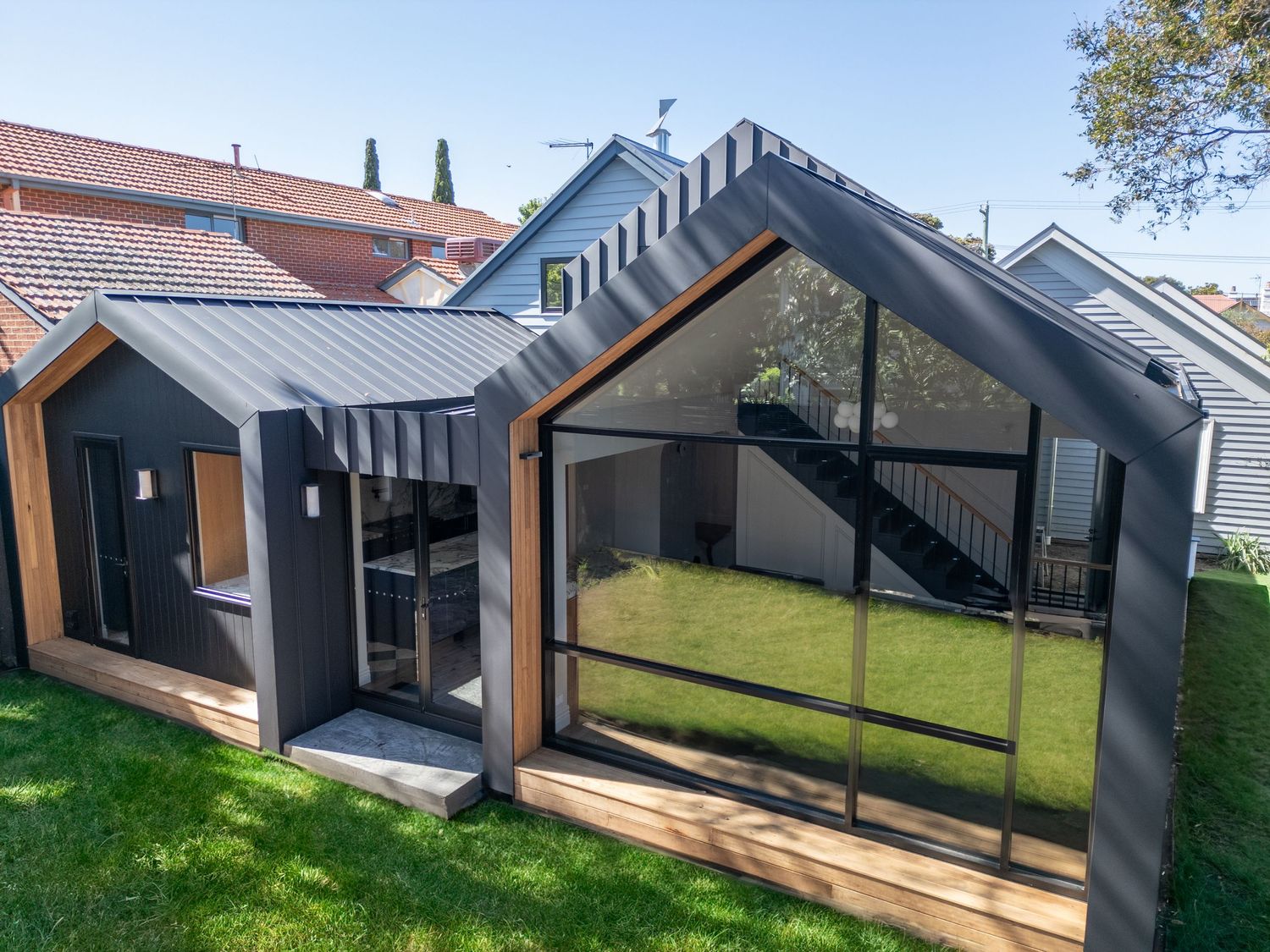 Modern backyard extension with black cladding and large glass panels connects to main house.