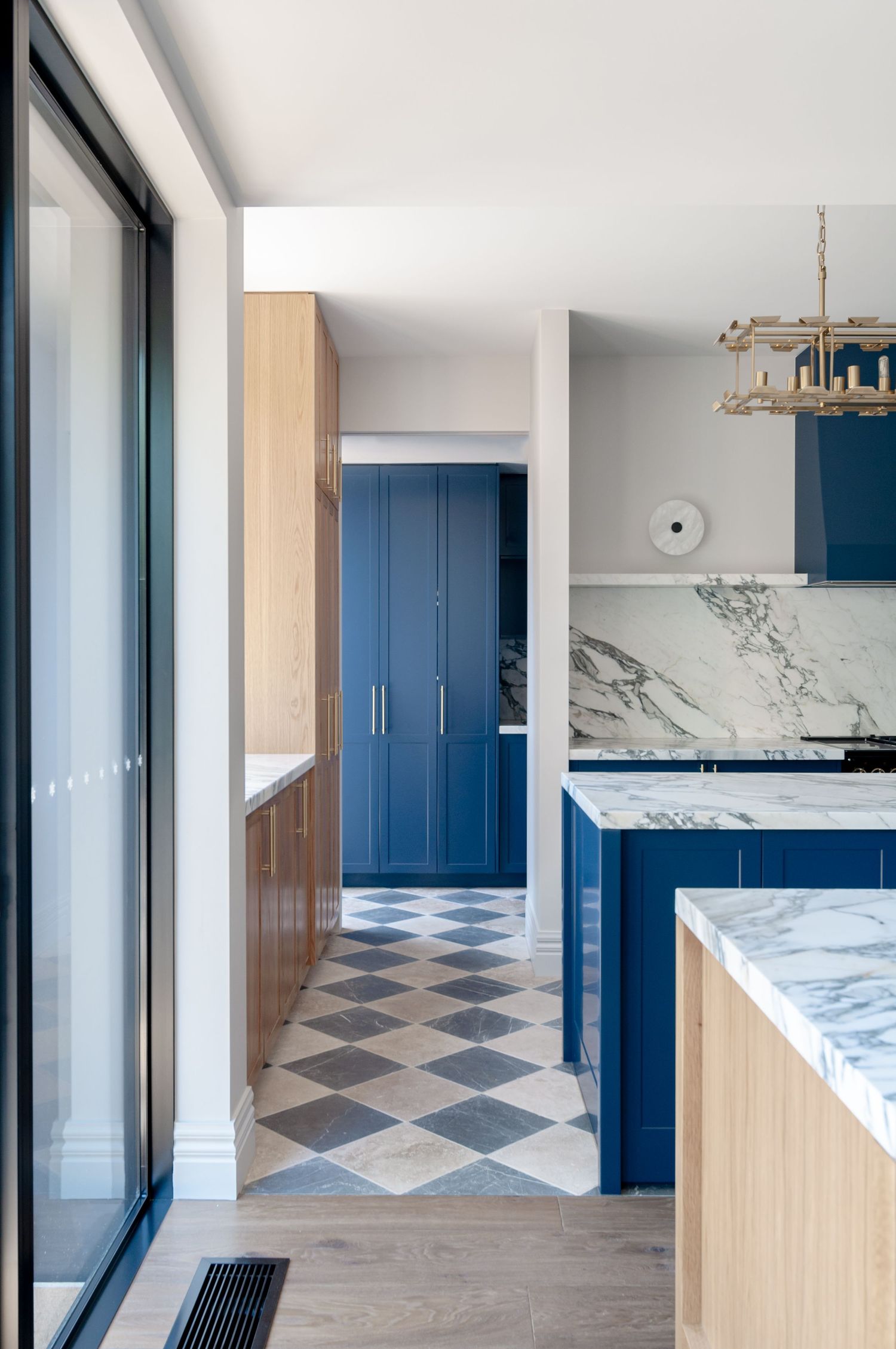 Contemporary kitchen interior with blue cabinets, marble countertops, and diagonal pattern flooring.