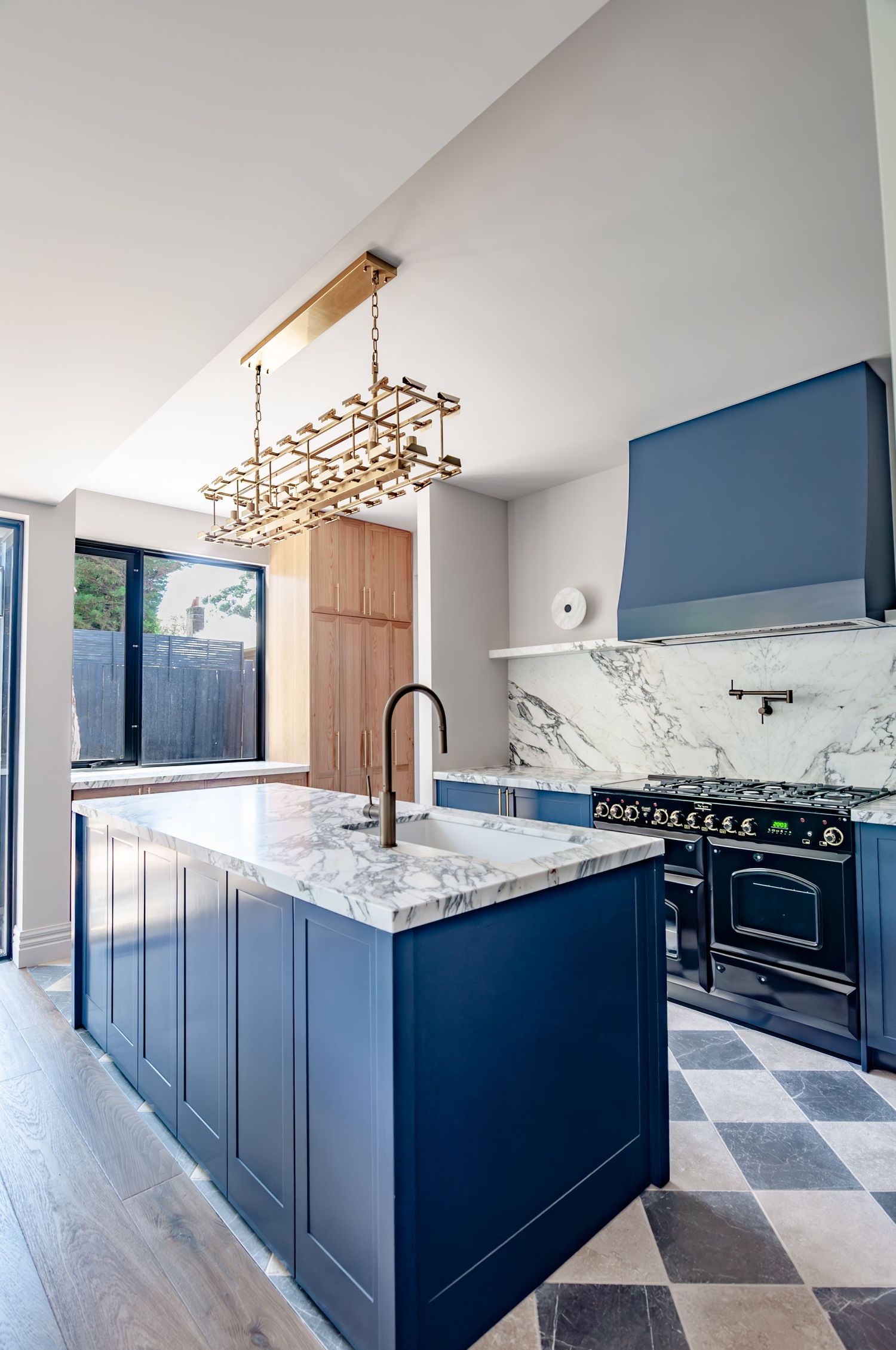 Modern kitchen featuring navy cabinets, marble counters and brass geometric chandelier.