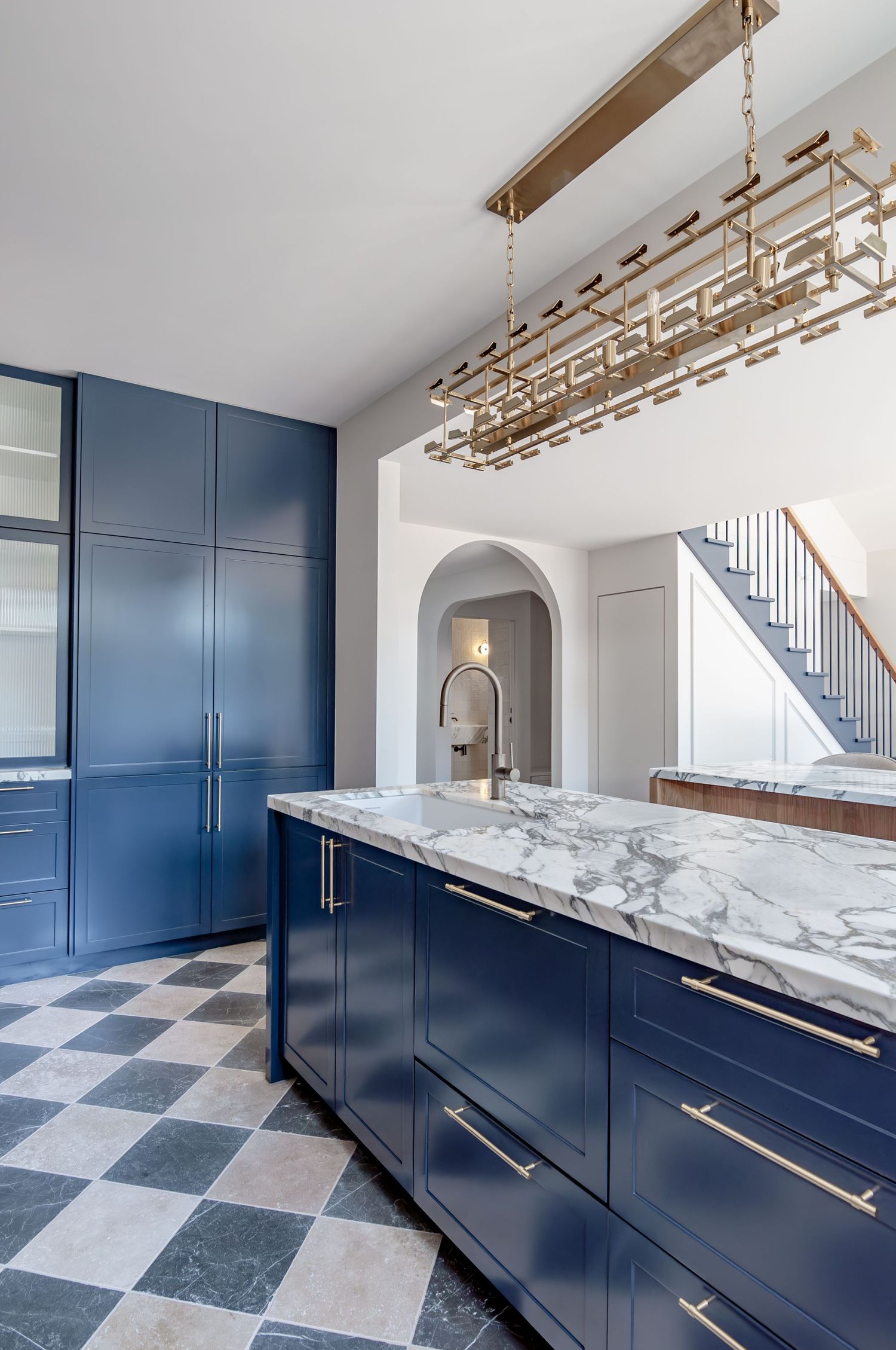 Navy blue kitchen with marble countertops, brass hardware and checkered floor pattern.