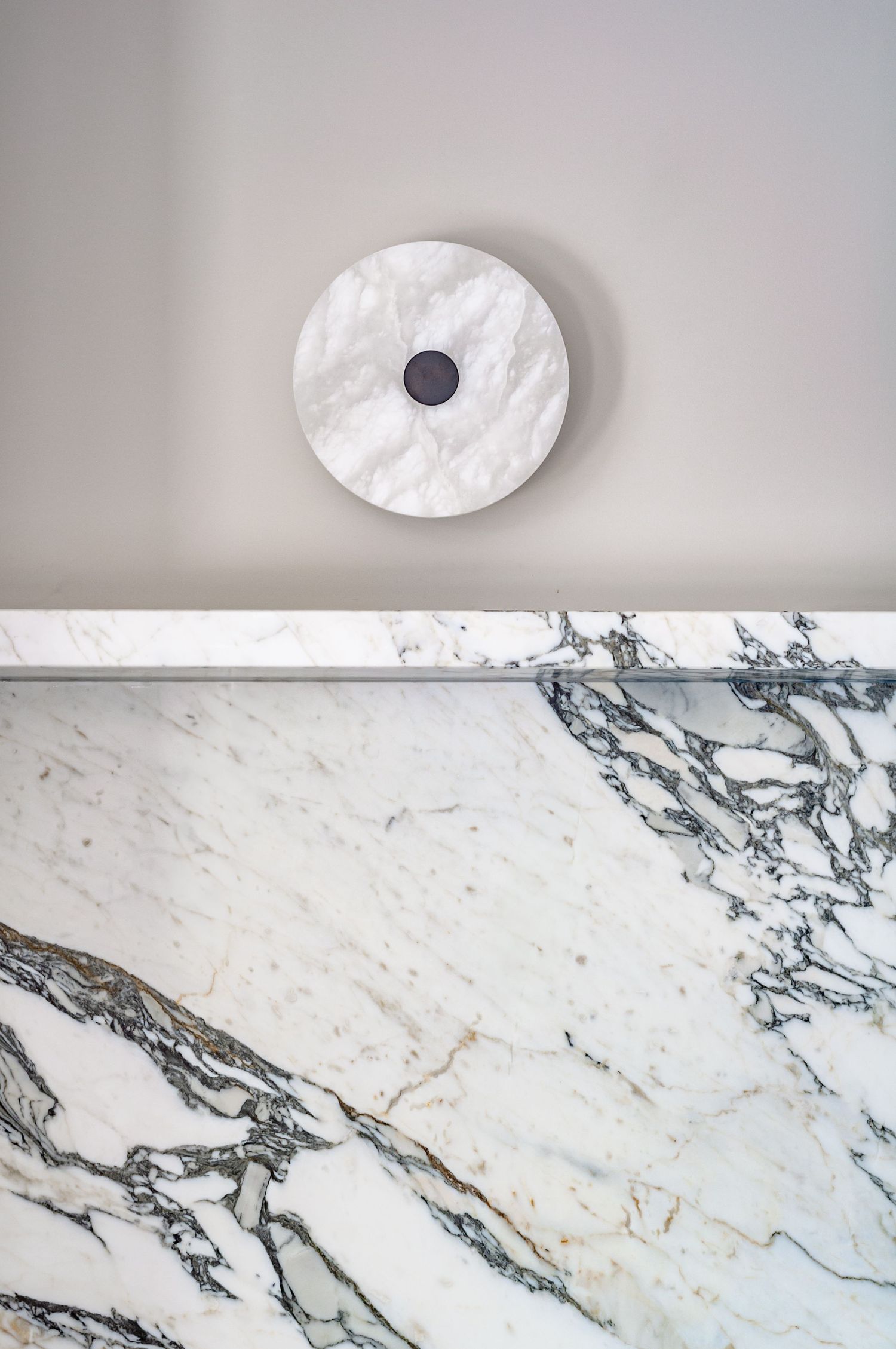 Circular marble wall light fixture above white marble wall panel with dramatic veining.