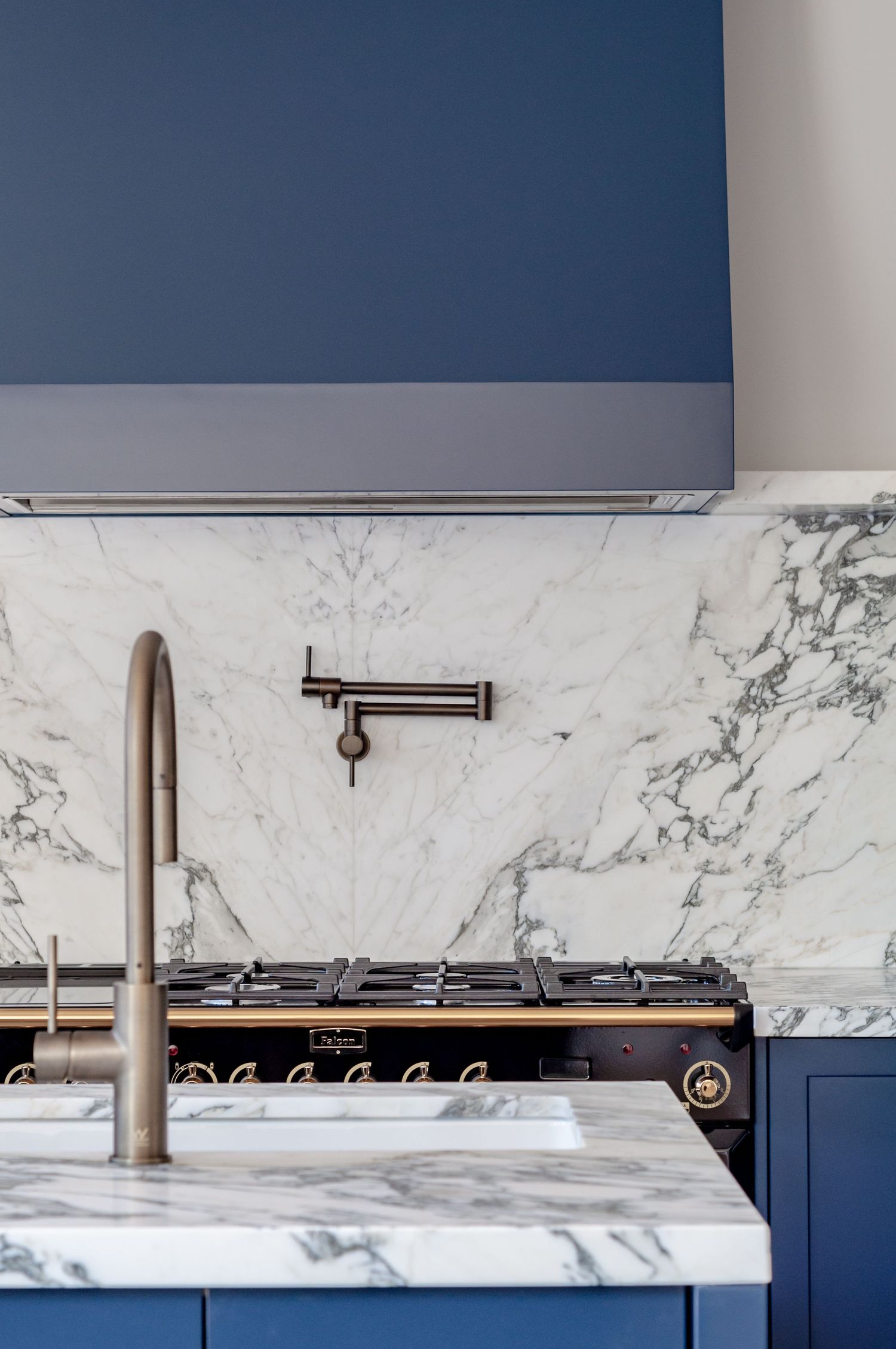 Luxury kitchen detail showing marble backsplash, pot filler faucet, and navy blue cabinetry with stainless steel appliances.