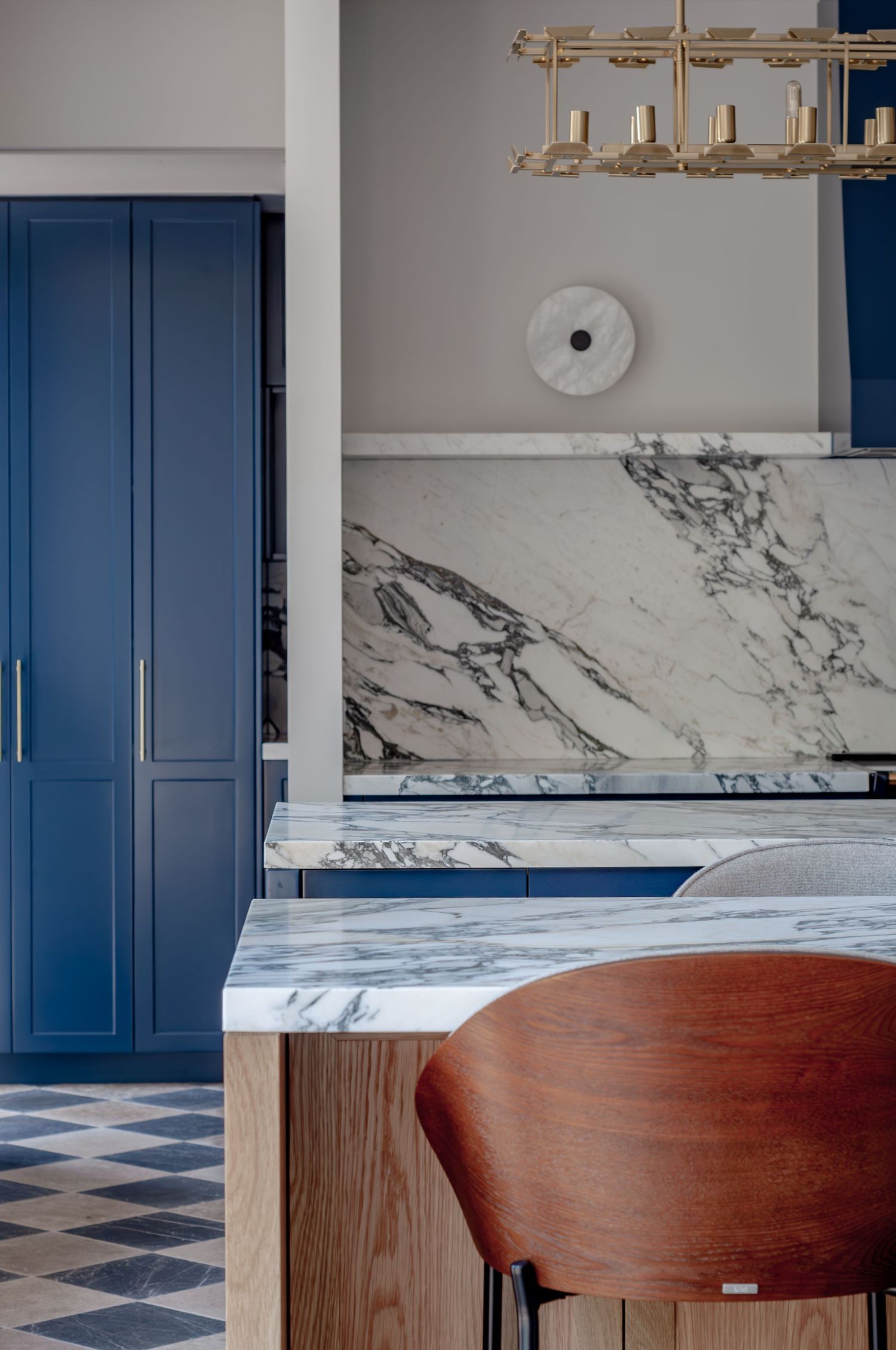 Modern kitchen design featuring navy blue cabinets, marble countertops, and a wooden bar stool against a checkered floor.