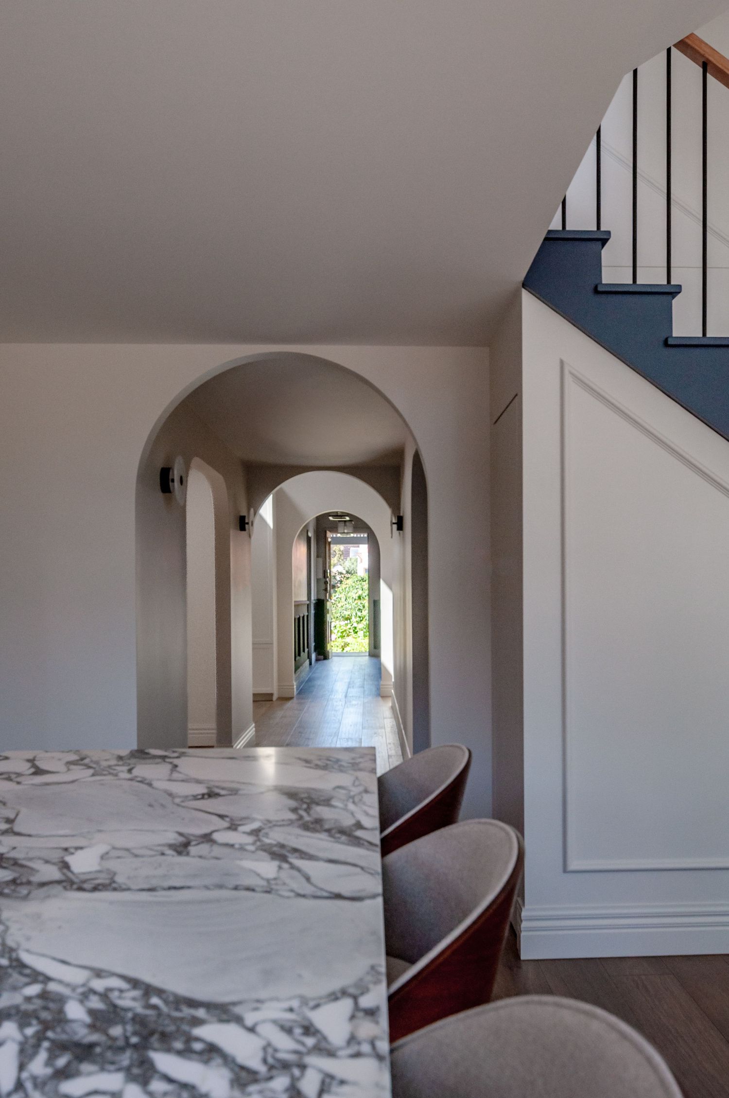 Elegant arched hallway with marble countertop and wooden floors leading to a bright sunlit doorway.