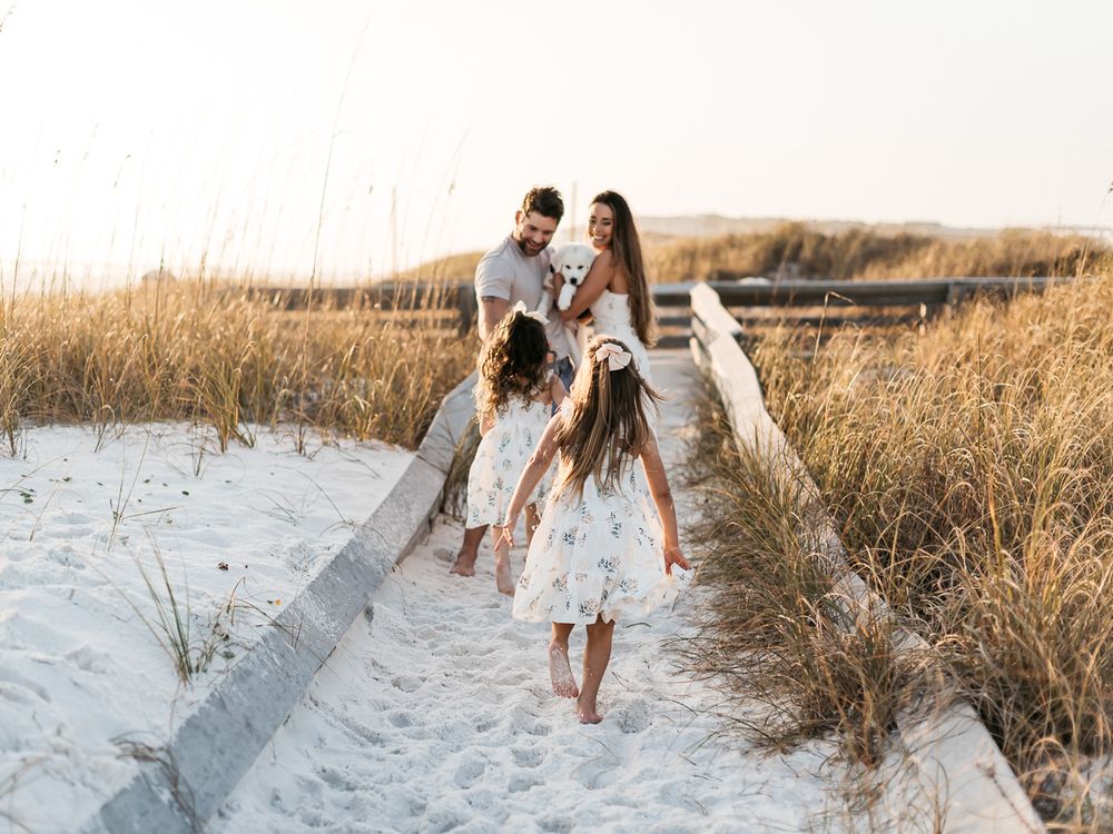 Couple enjoying a romantic sunset photoshoot at a beach with golden light filtering through sea grass.
