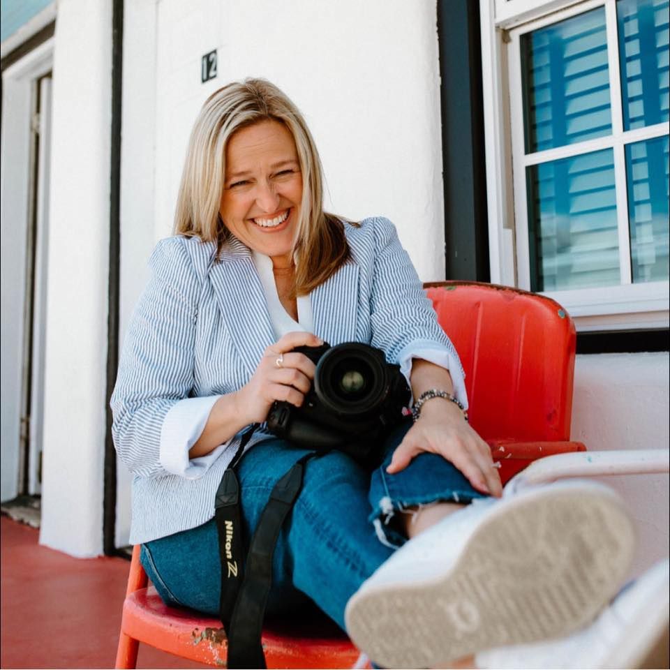 A photographer sits in a red chair outdoors while reviewing images on their camera.