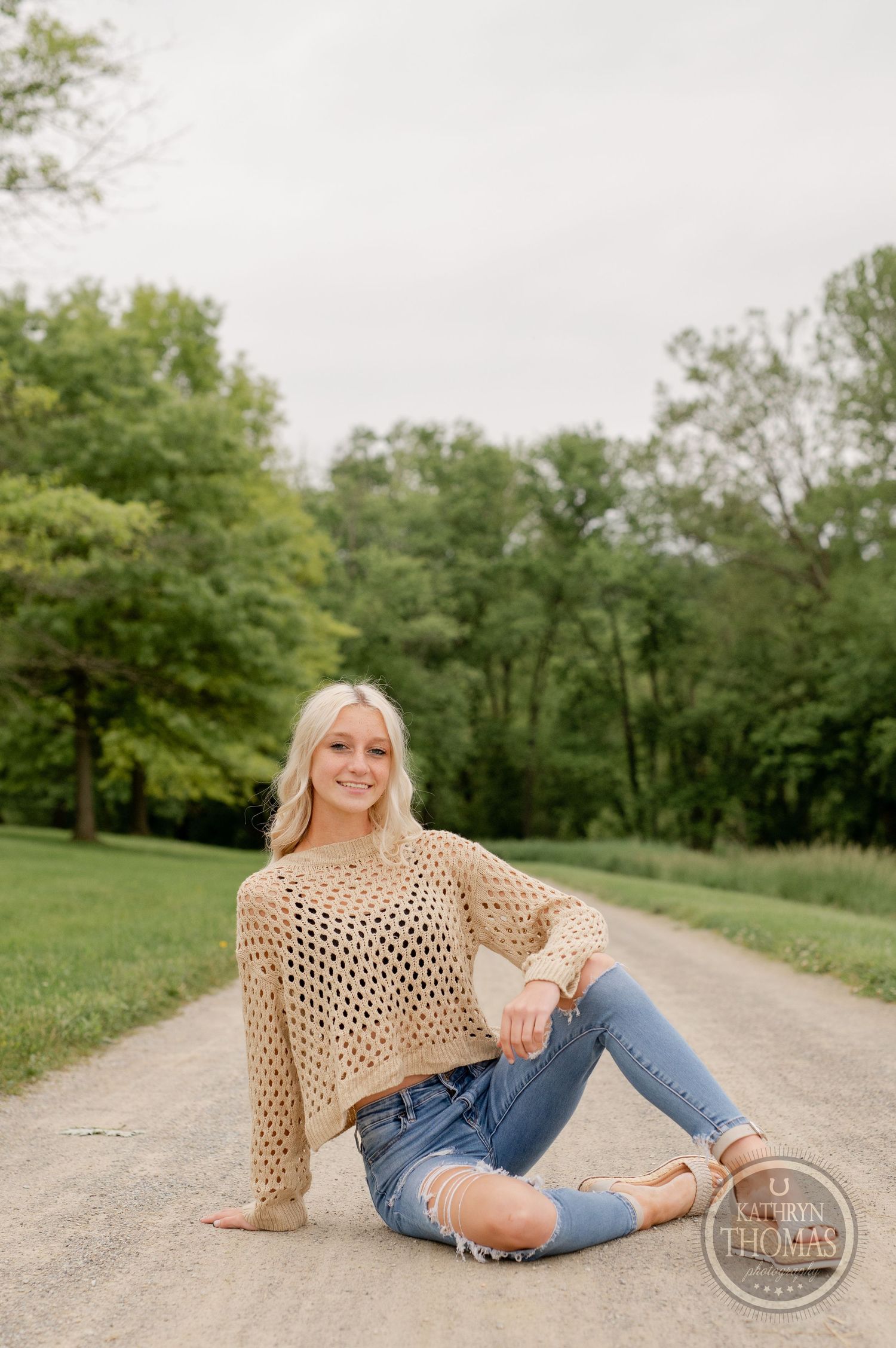 Relaxed countryside fashion pose on dirt path wearing distressed denim and knit sweater.