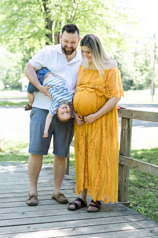 Family shares playful moment on wooden bridge with toddler hanging upside down.