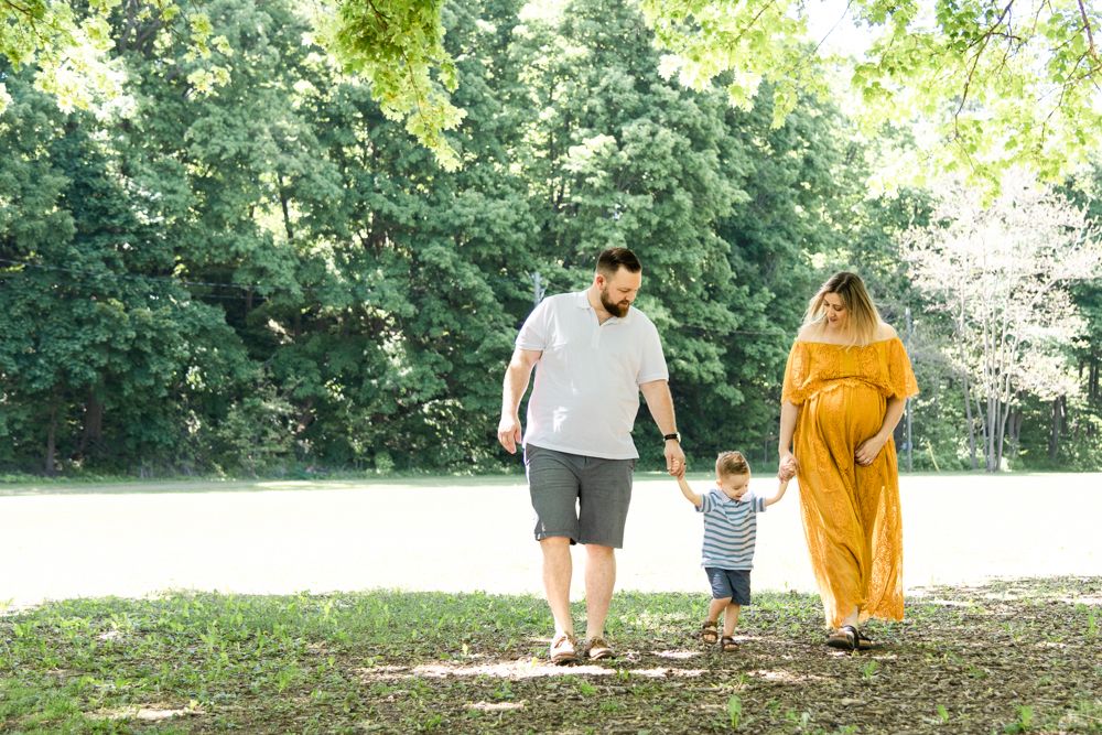 Family walks together on wooded path with young child between parents.