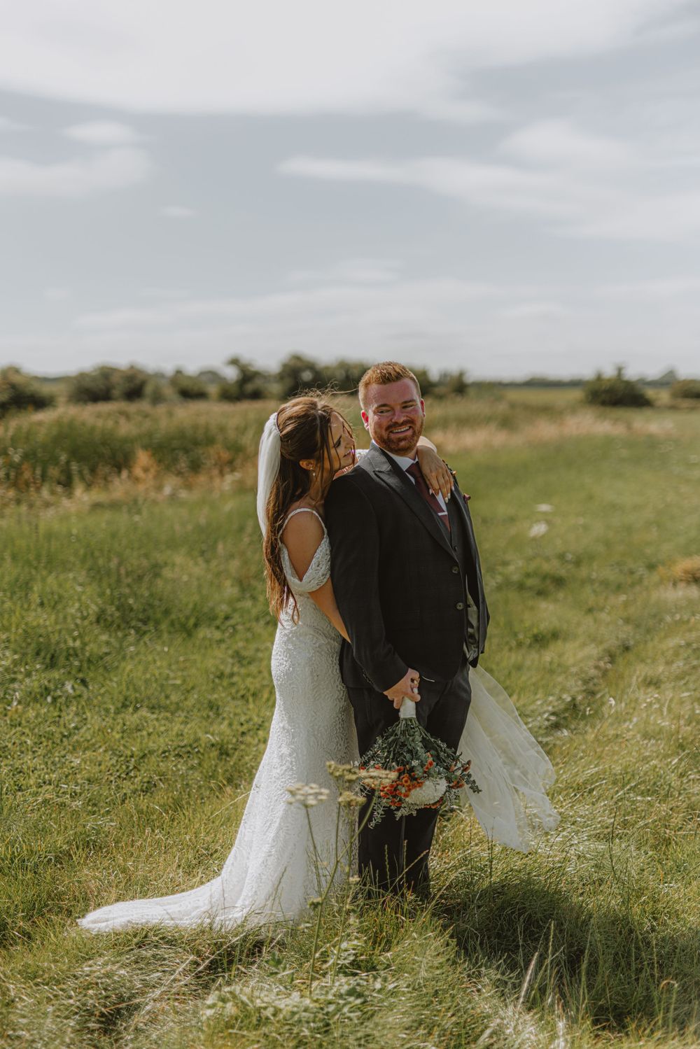Wedding couple popping champagne together in a sunlit meadow.