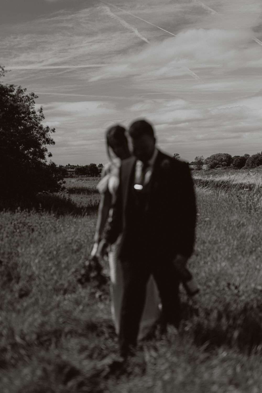 Black and white silhouette of newlyweds walking through a rural field.