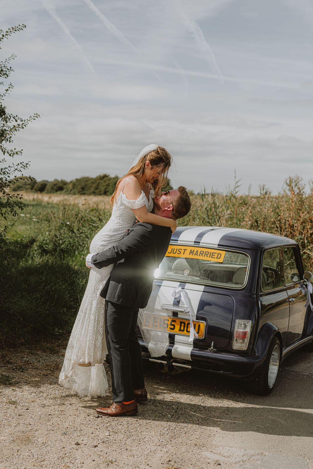 A vintage car decorated for a wedding celebration parked on a gravel path.