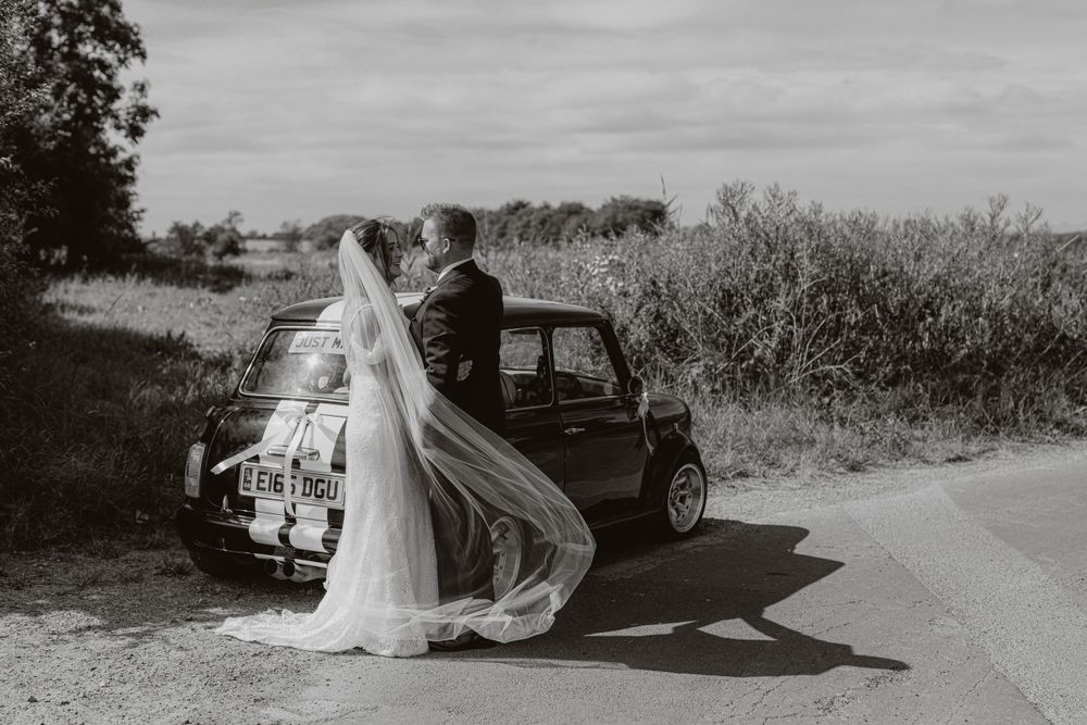 A classic car with racing stripes photographed in black and white on a country road.