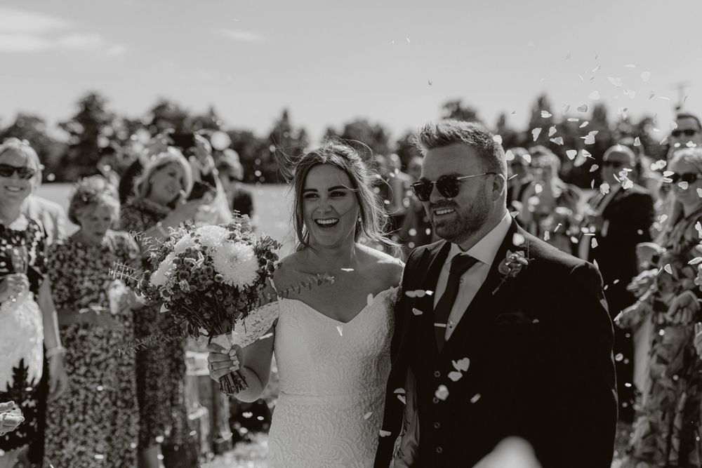 Joyful outdoor wedding celebration with guests throwing confetti.