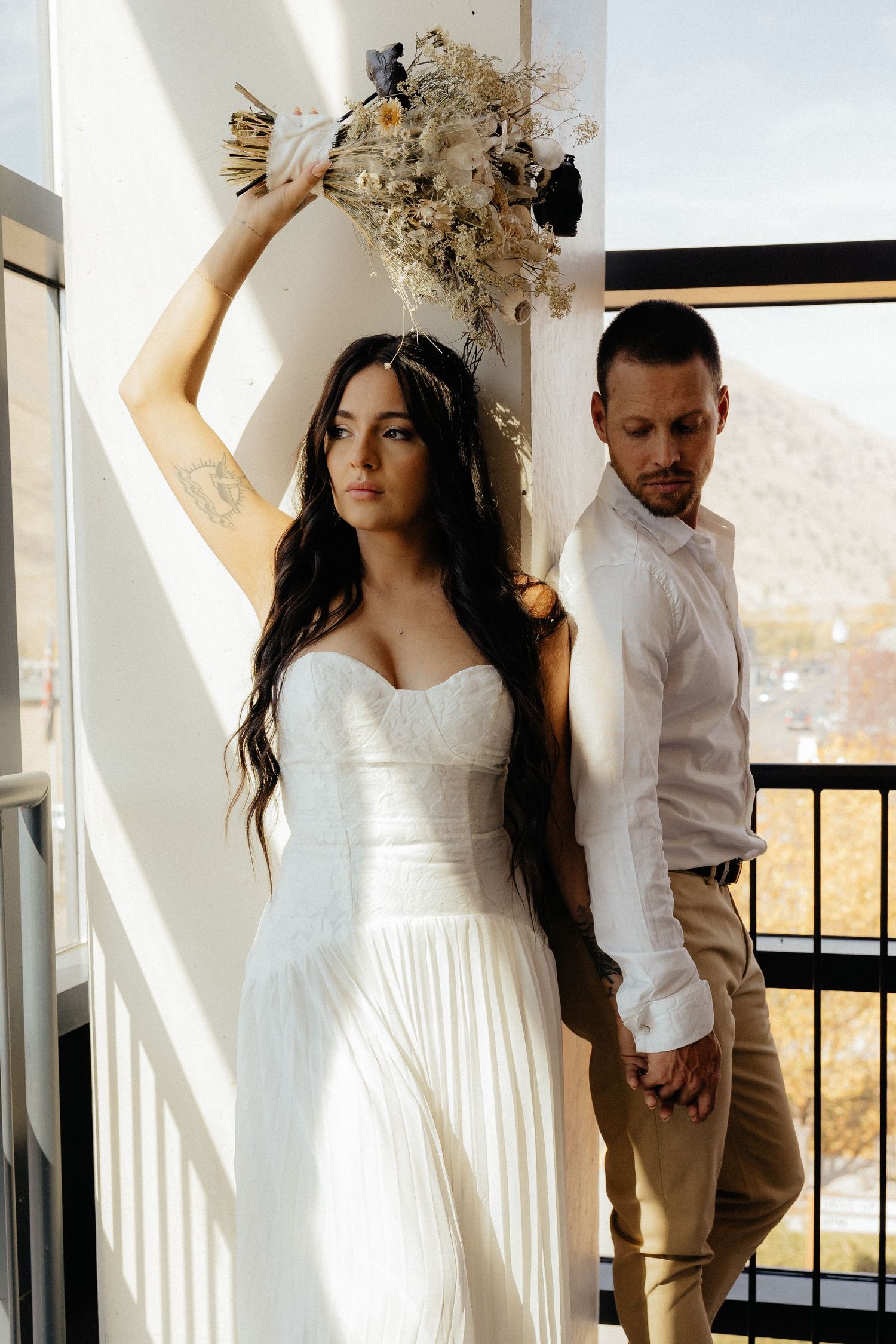 Artistic wedding portrait on balcony with dried flower bouquet held high.