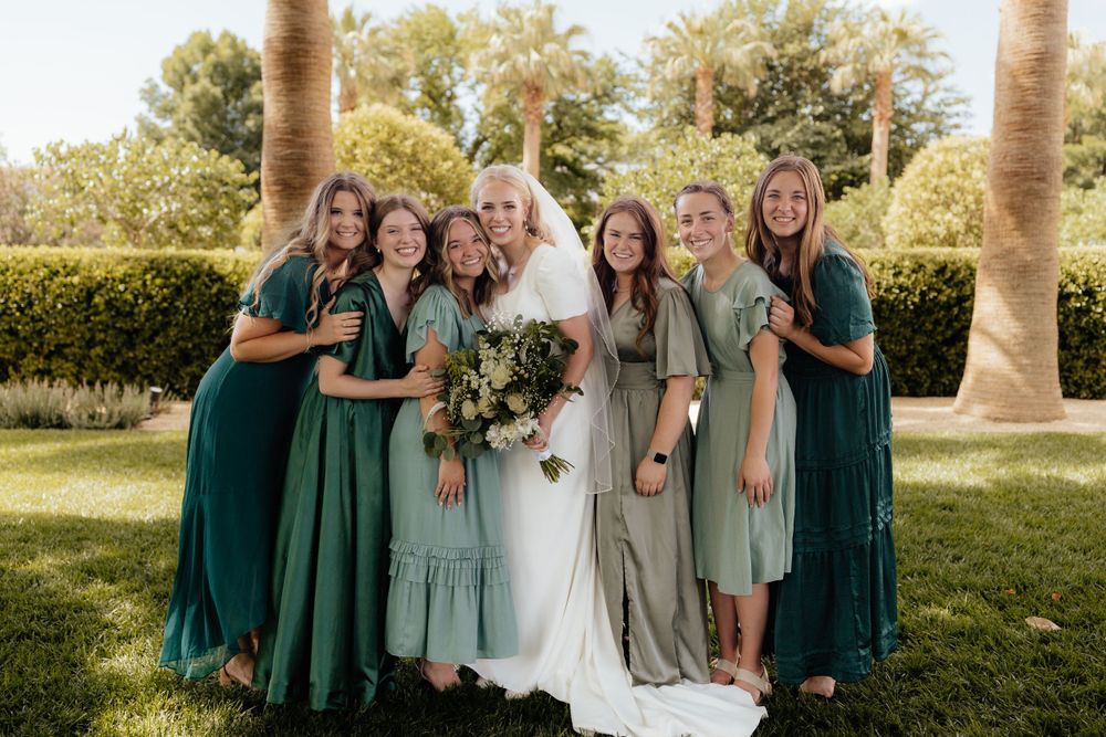 Bride with six bridesmaids in green dresses celebrating outdoors among palm trees.