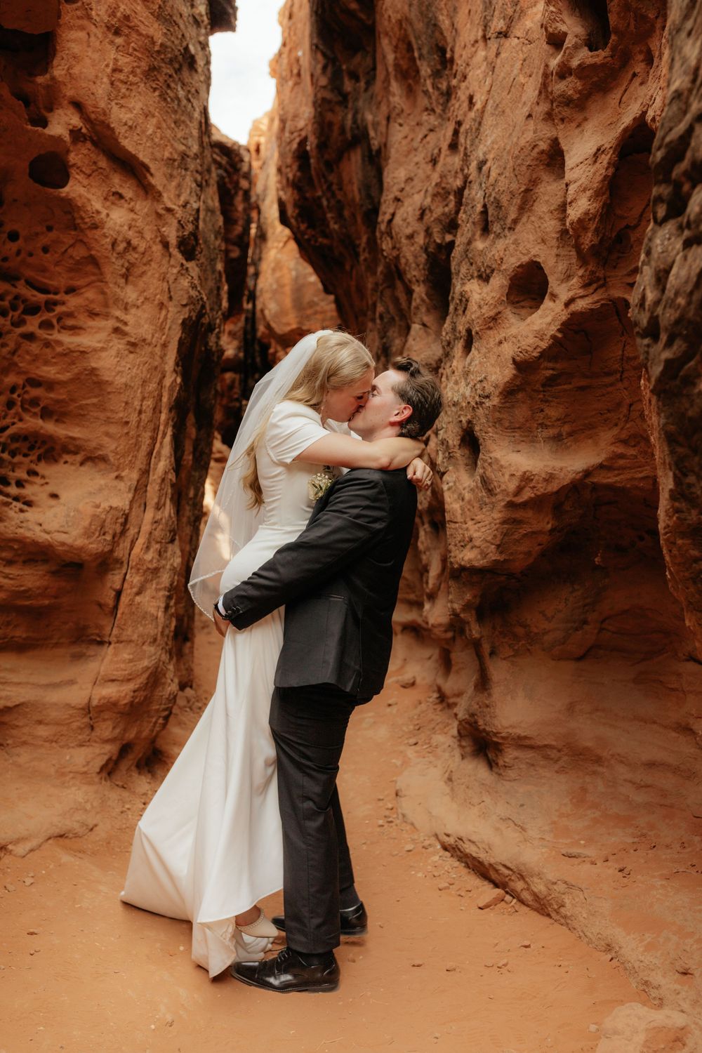 Bride and groom share romantic kiss in stunning red rock canyon landscape.