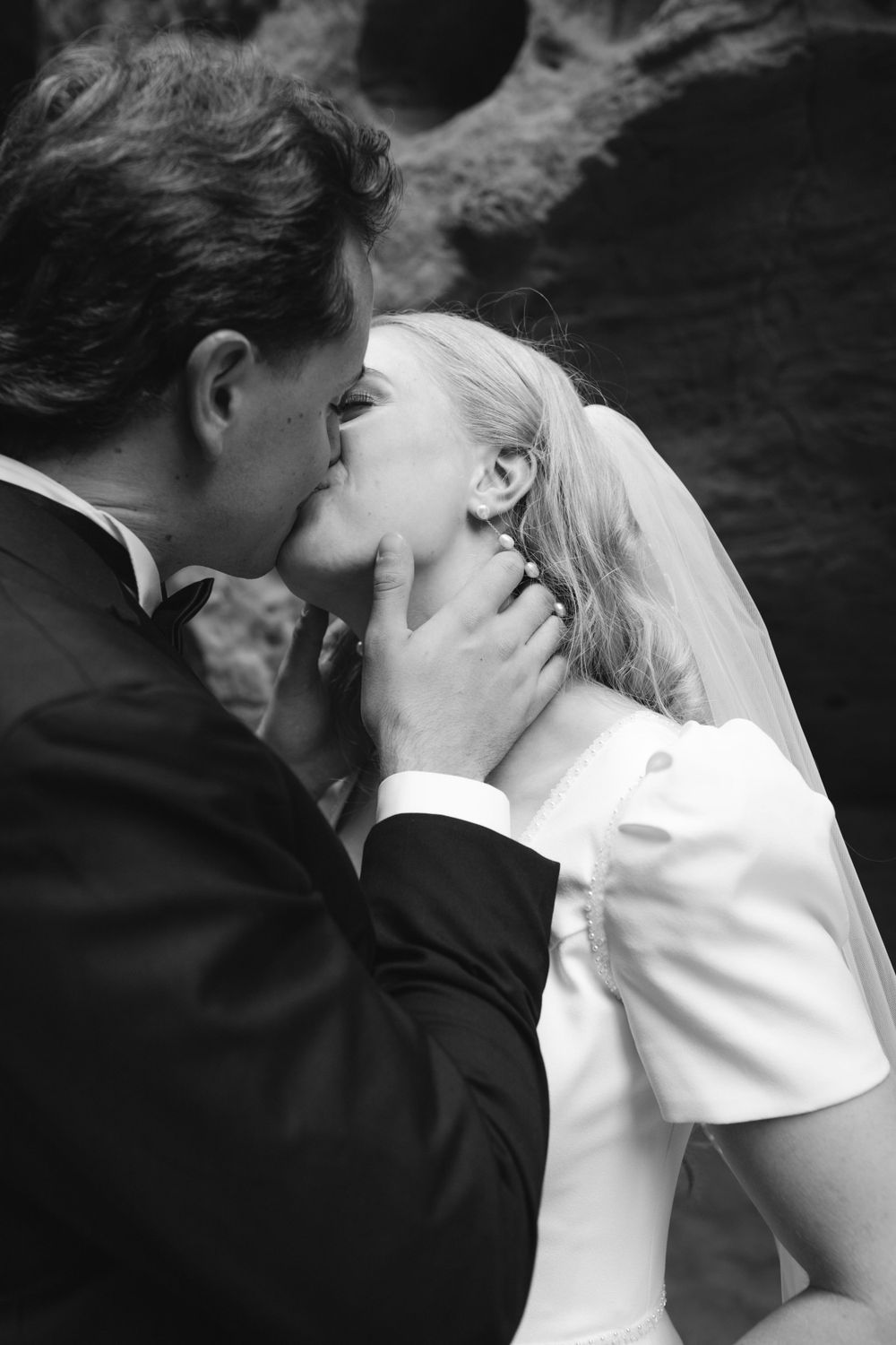 Black and white photo of groom tenderly kissing bride in wedding attire.