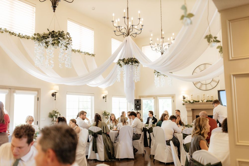 Wedding reception guests gathered under white fabric ceiling draping with chandelier and greenery decor.