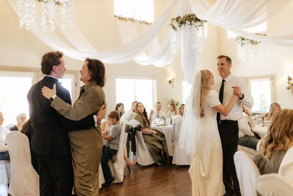 Bride and groom sharing first dance with parents at elegant white wedding reception venue.