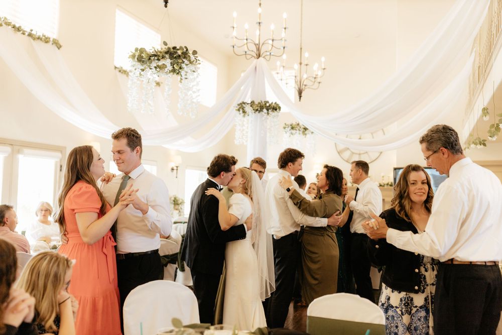 Wedding guests and newlyweds dancing joyfully in elegantly draped reception venue.
