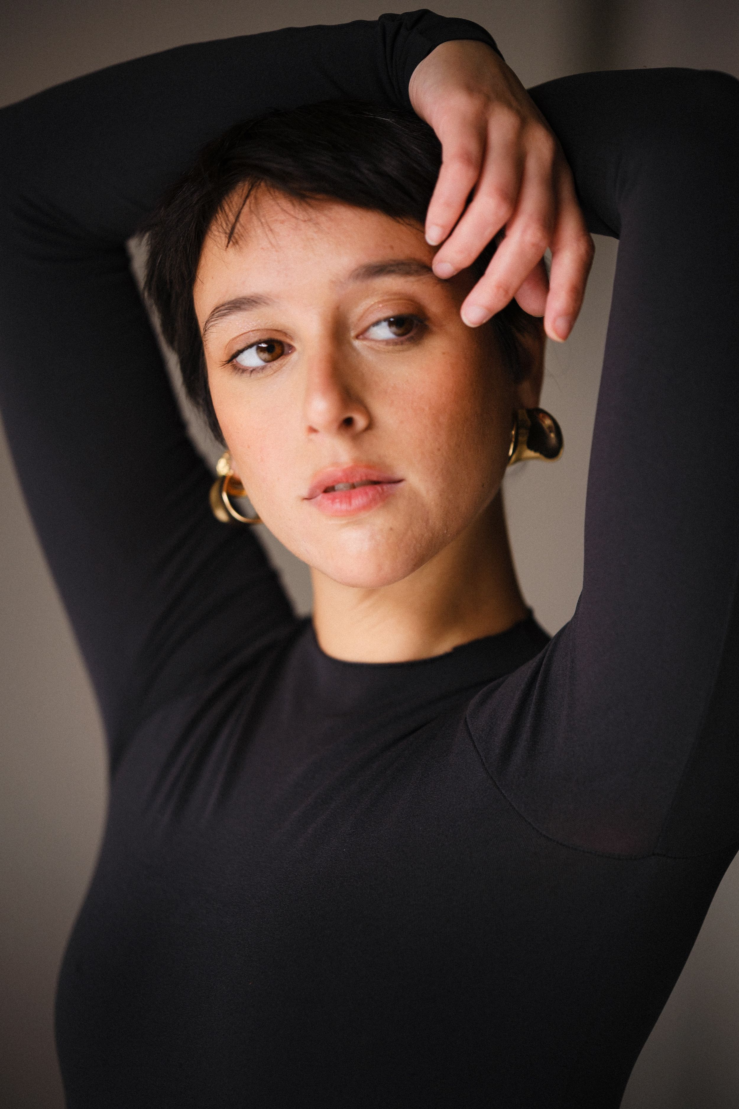 Artistic headshots with raised arms in black turtleneck against dark background.