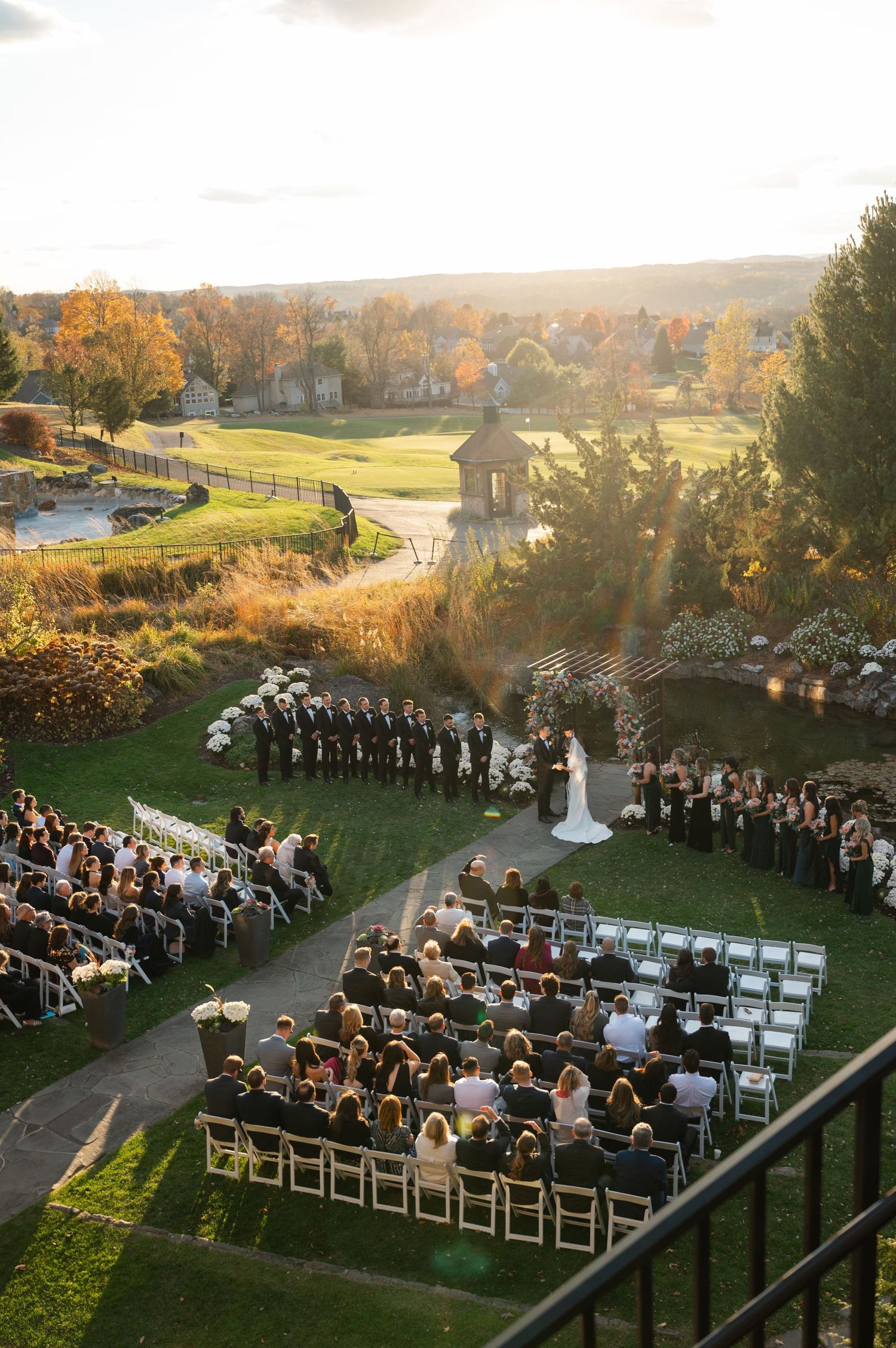 Wedding party in pink and black attire poses together on outdoor steps during celebration.