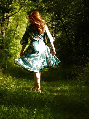 A flowing dress twirls in a sunlit forest clearing with lush green foliage.