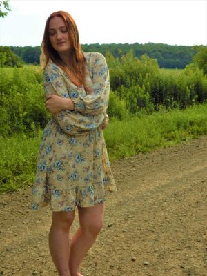 A floral dress catches the breeze on a dirt path with green hills in the background.