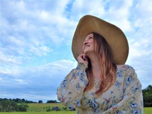 A wide-brimmed straw hat stands out against dramatic cloudy skies in a rural setting.