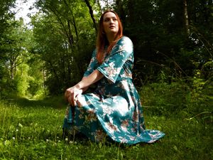 A flowing dress creates movement in a serene forest setting with dappled sunlight.