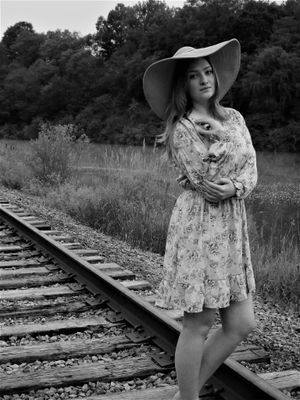 A vintage-style photoshoot on abandoned railroad tracks with a floral dress and wide-brimmed hat.
