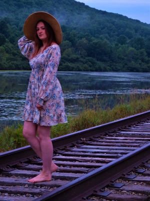 Railroad tracks beside a serene lake at dusk with mountains in the background.
