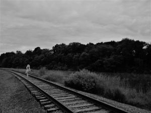 Railroad tracks curving through a misty rural landscape in black and white.
