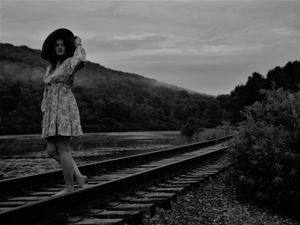Moody black and white photo of a person walking along railroad tracks with trees in the background.