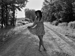A figure in silhouette walks along a dirt path surrounded by trees and greenery.