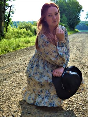 A floral dress and sunhat create a vintage aesthetic on a dirt path in nature.