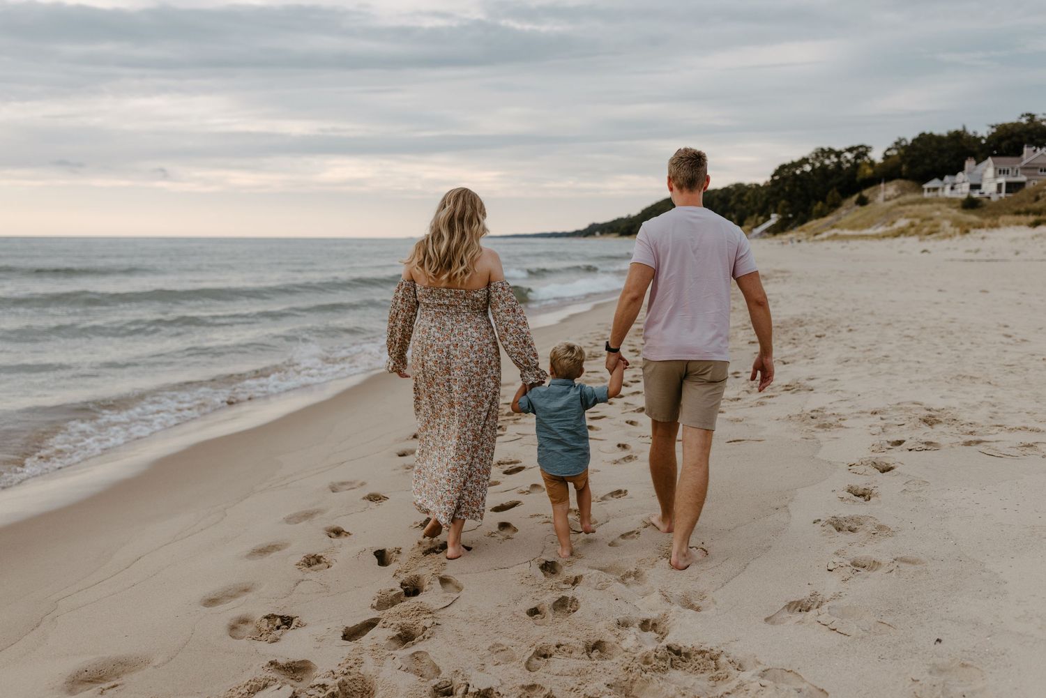 A family walks together on a sandy beach, holding hands and enjoying the scenic ocean view. Fort Worth Texas family photographer.