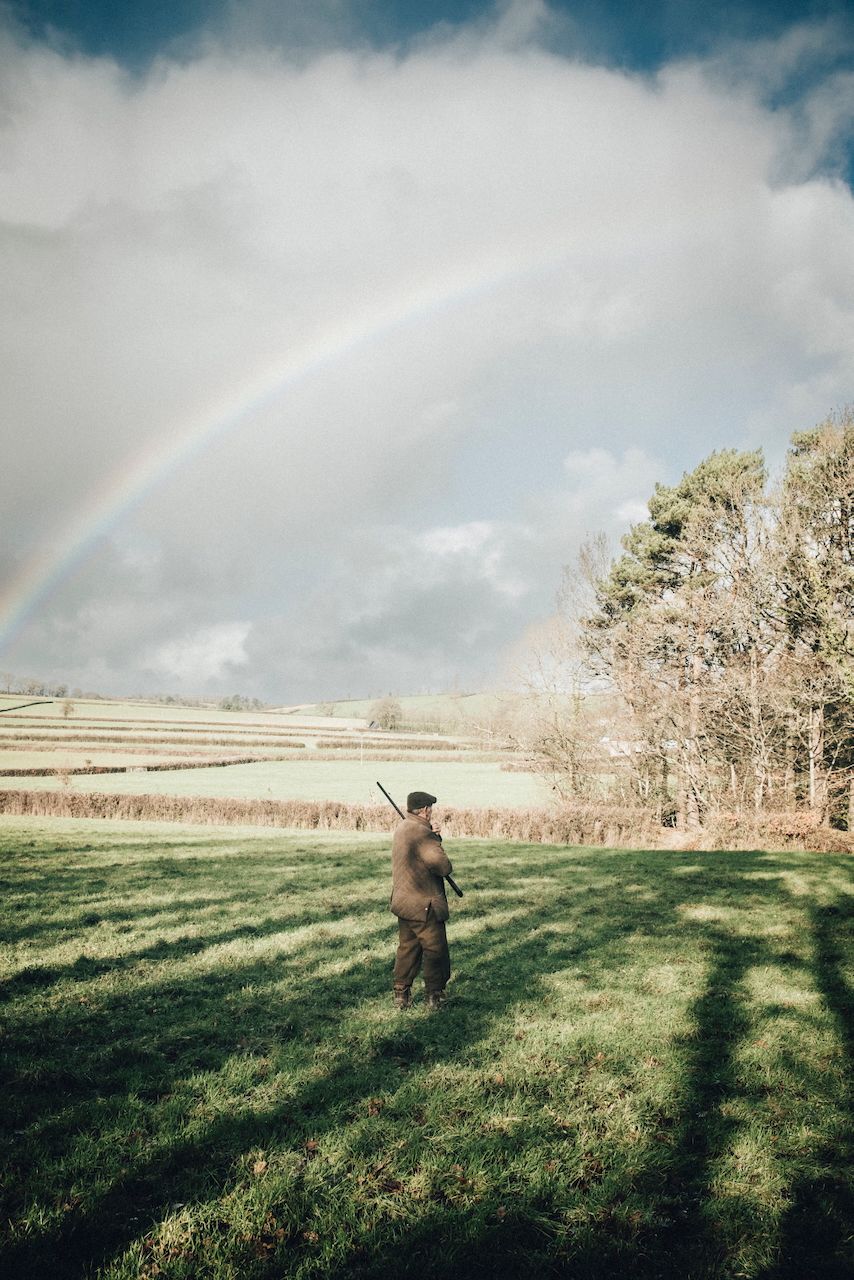 Pheasant shooting reportage photo of gun shooting high birds over exmoor with rainbow in stormy sky