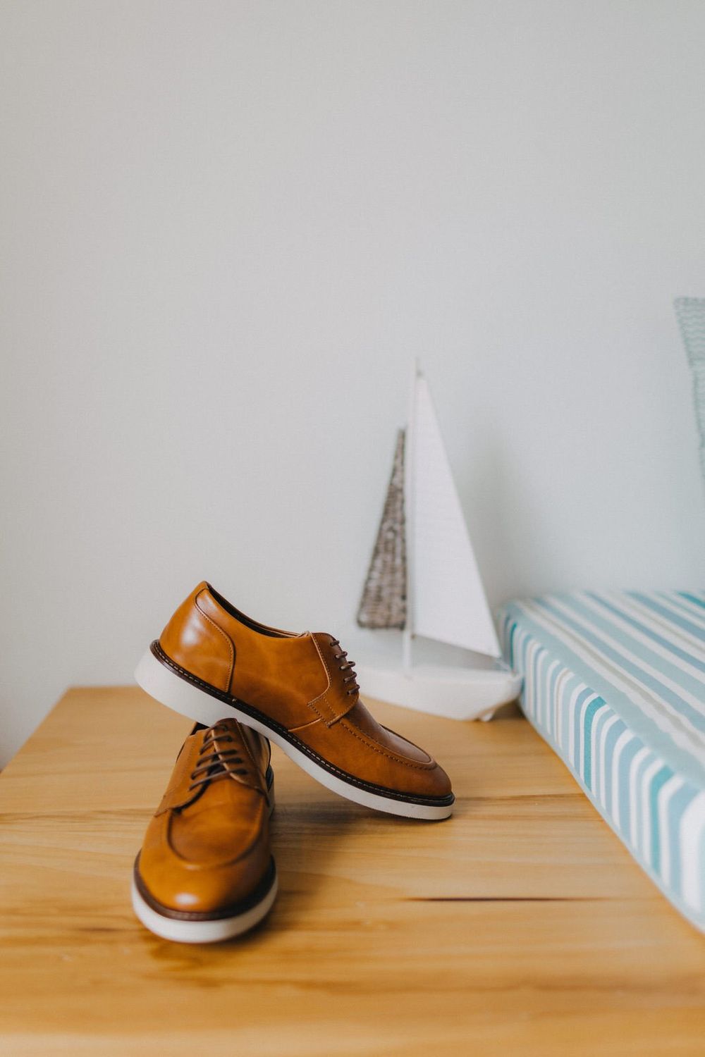 Pair of brown leather oxford shoes with white soles on wooden table against light gray wall.