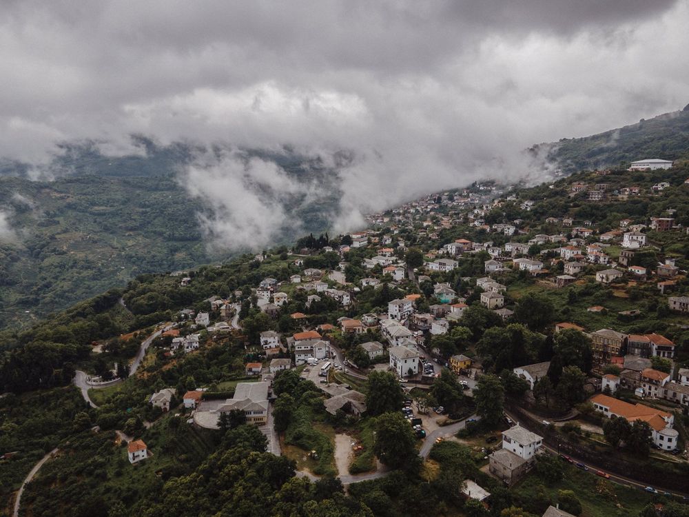Aerial view of hillside village with white houses nestled in foggy mountains.