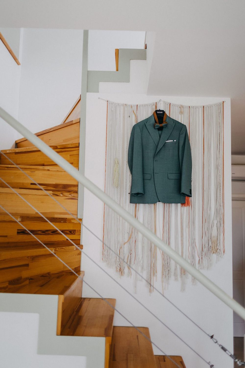 Modern staircase with wooden steps and white walls featuring a green suit jacket hanging on display.