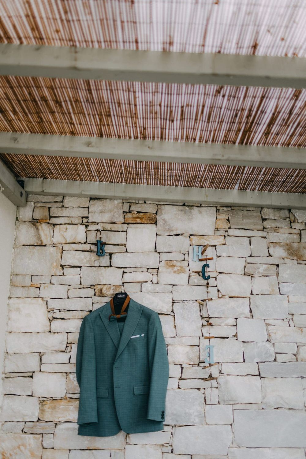 Green blazer hanging against rustic stone wall with bamboo ceiling detail.