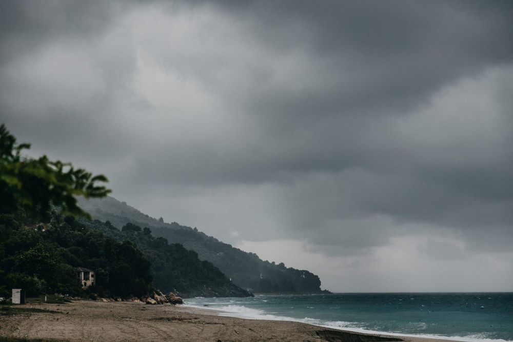 Dramatic stormy coastline with mountains and dark clouds over beach.