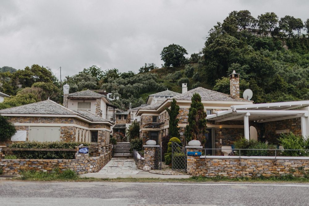 Large stone mansion with multiple buildings and landscaping nestled on hillside.