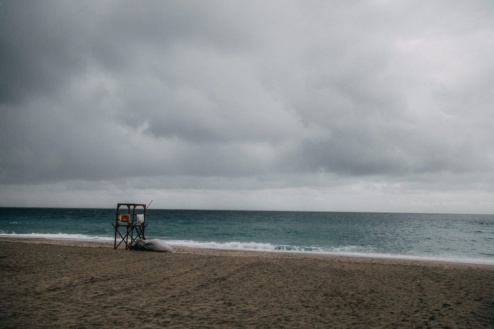 Empty beach with lifeguard tower under moody gray skies and turquoise waters.