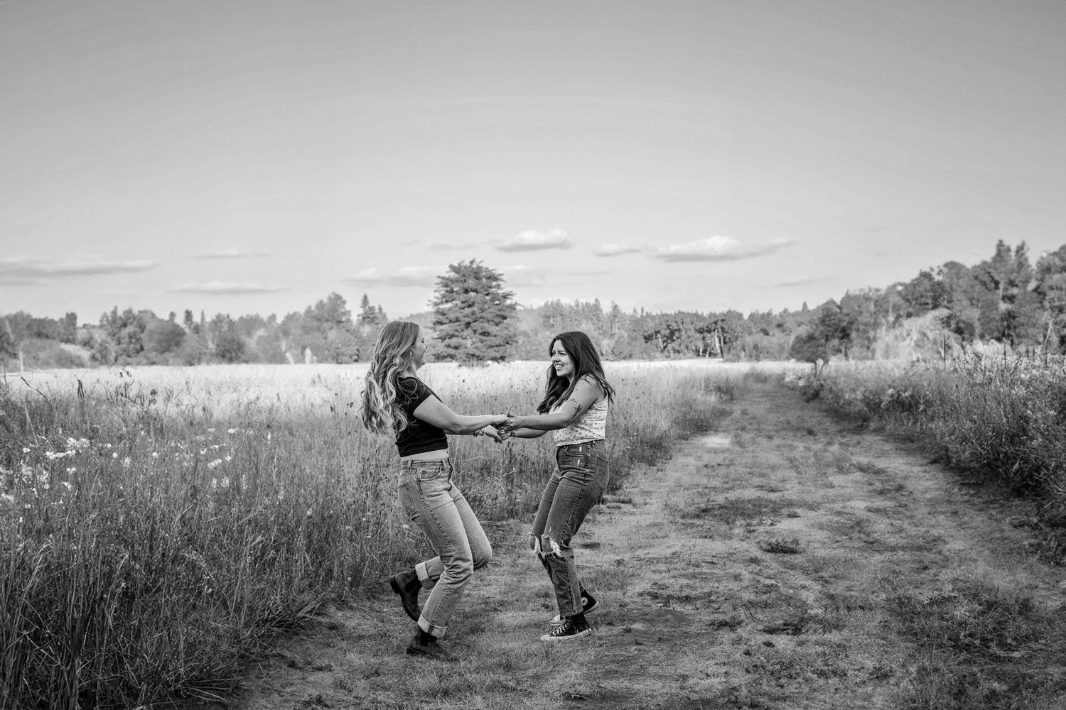 black and white image of two girls holding hands and spinning along a trail in a field