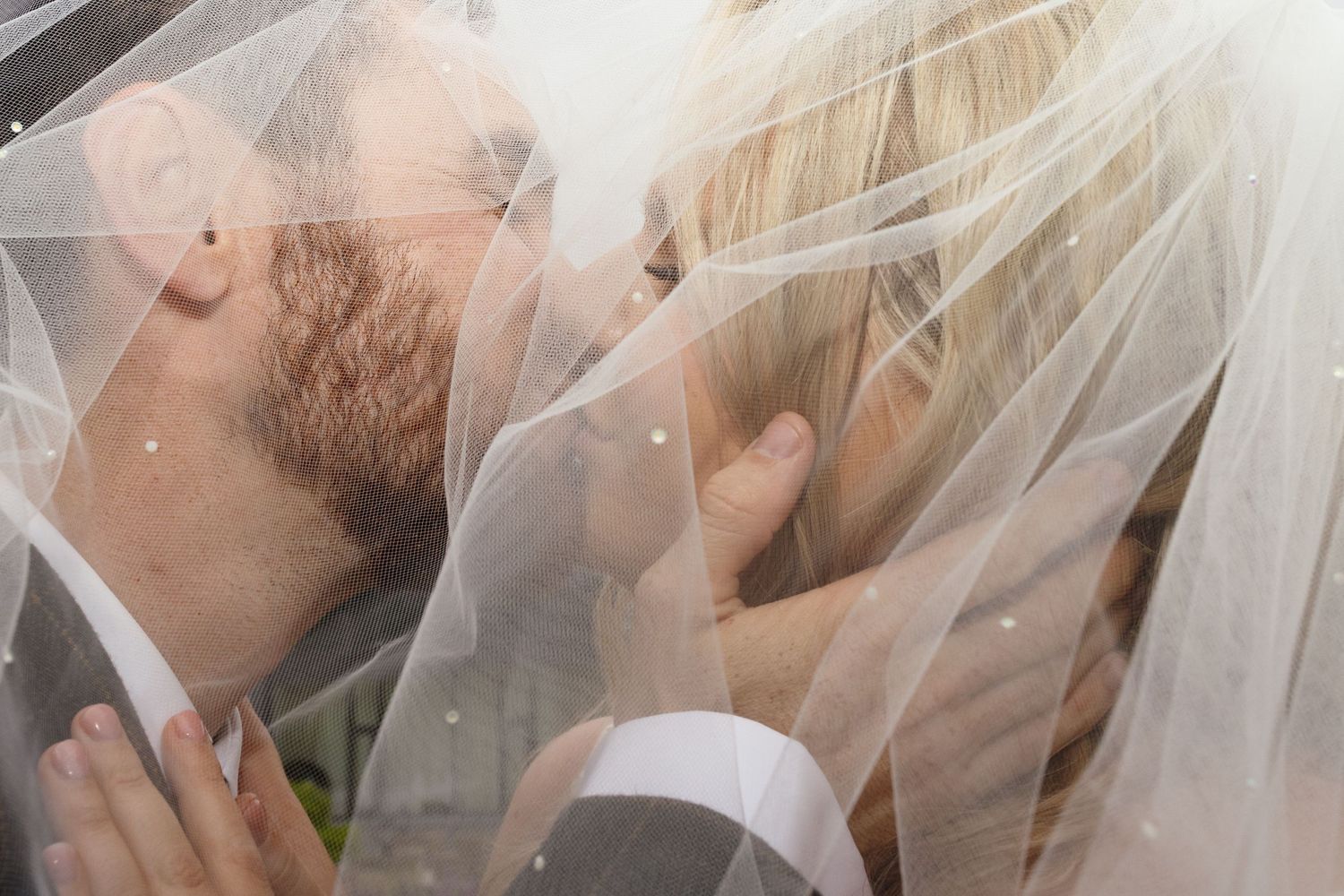 A bride and groom share a romantic kiss under a flowing white veil during their wedding ceremony.