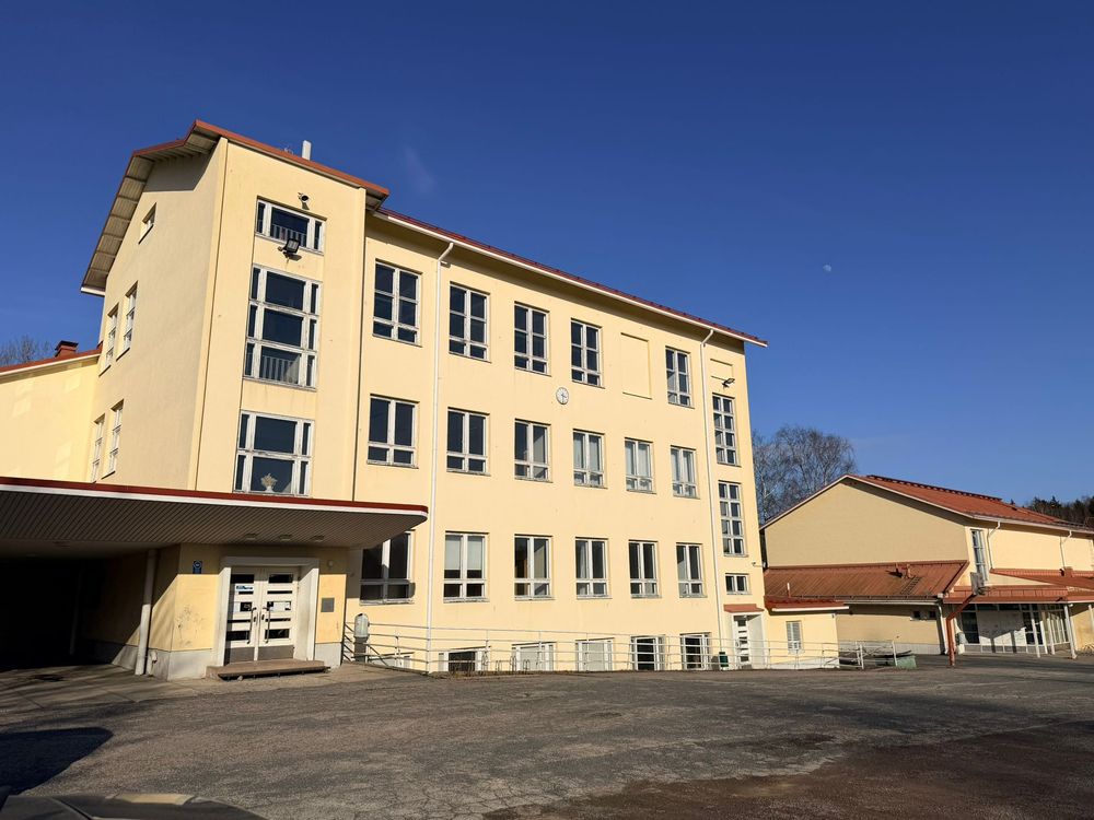 Large yellow three-story school building with a clear blue sky and empty courtyard.